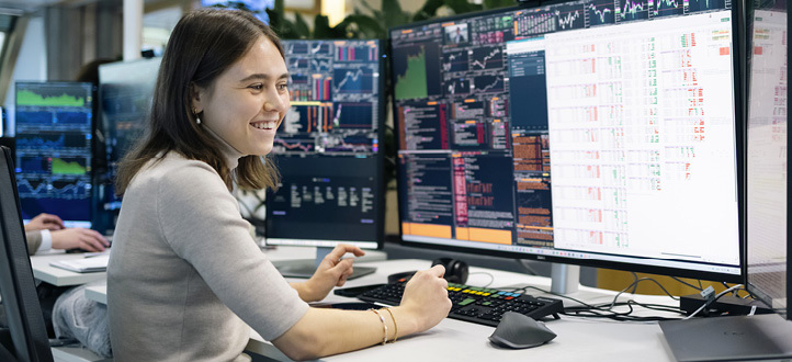 Ansatt ved Oslo-kontoret arbeider foran flere skjermer med markedsdata og analyser i et åpent kontorlandskap.