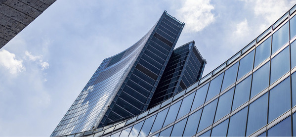 Utsikt opp mot moderne glasskledde kontorbygg mot blå himmel.