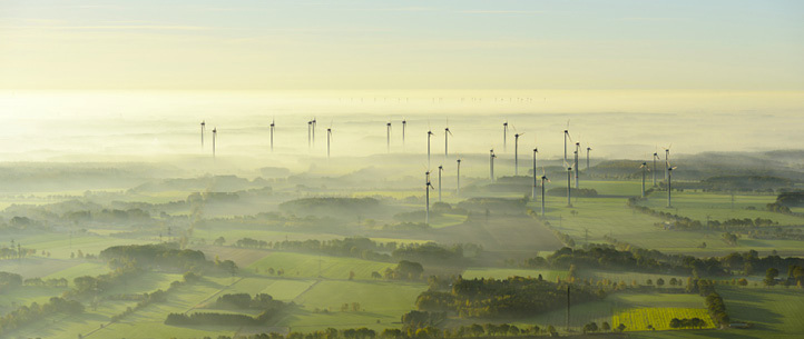 Wind turbines spread across farmland in early morning mist.