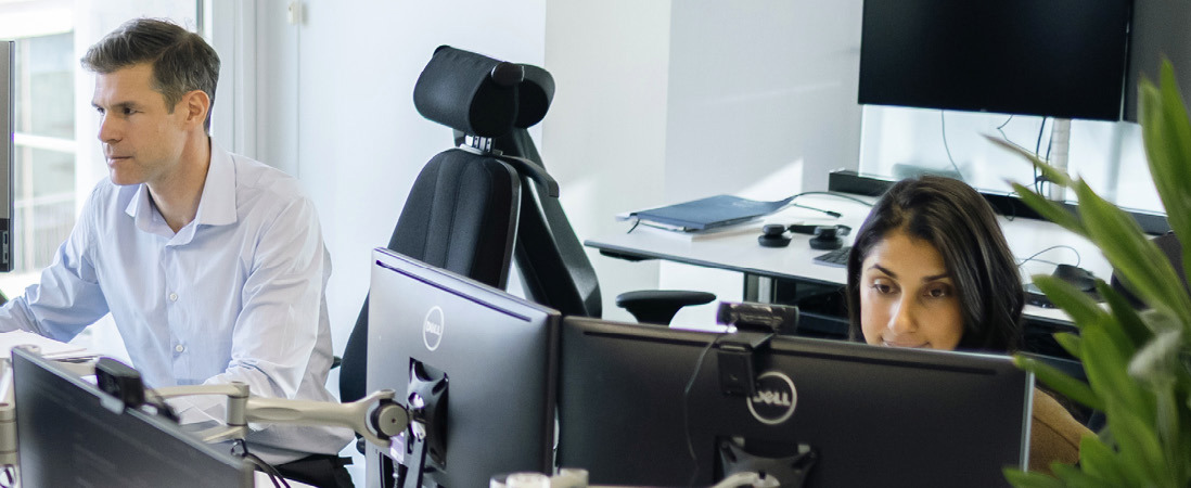To ansatte som arbeider ved dataskjermer i et kontorlandskap.